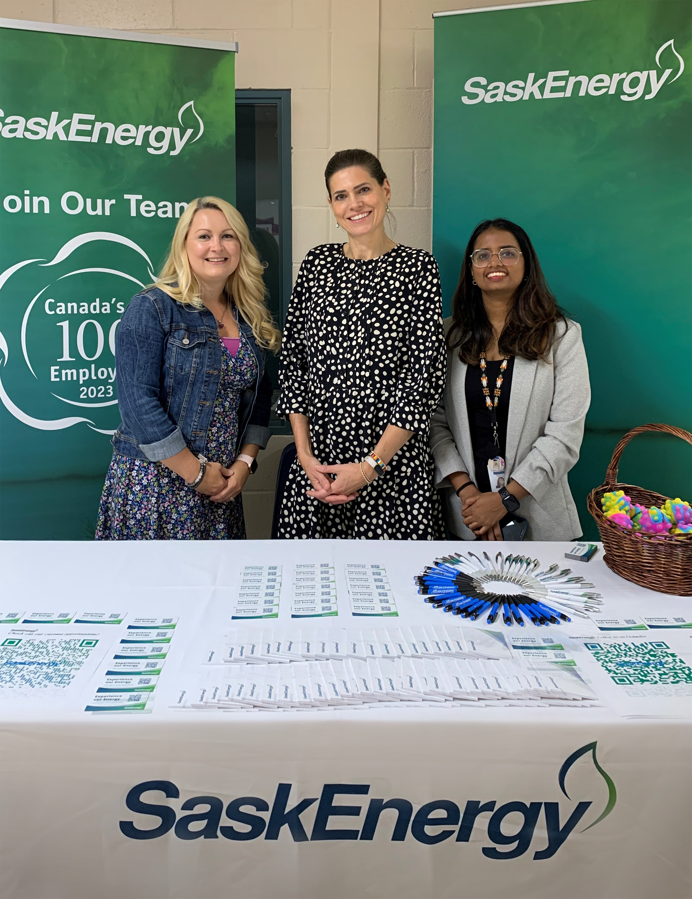 Three people stand at a booth at a career fair.