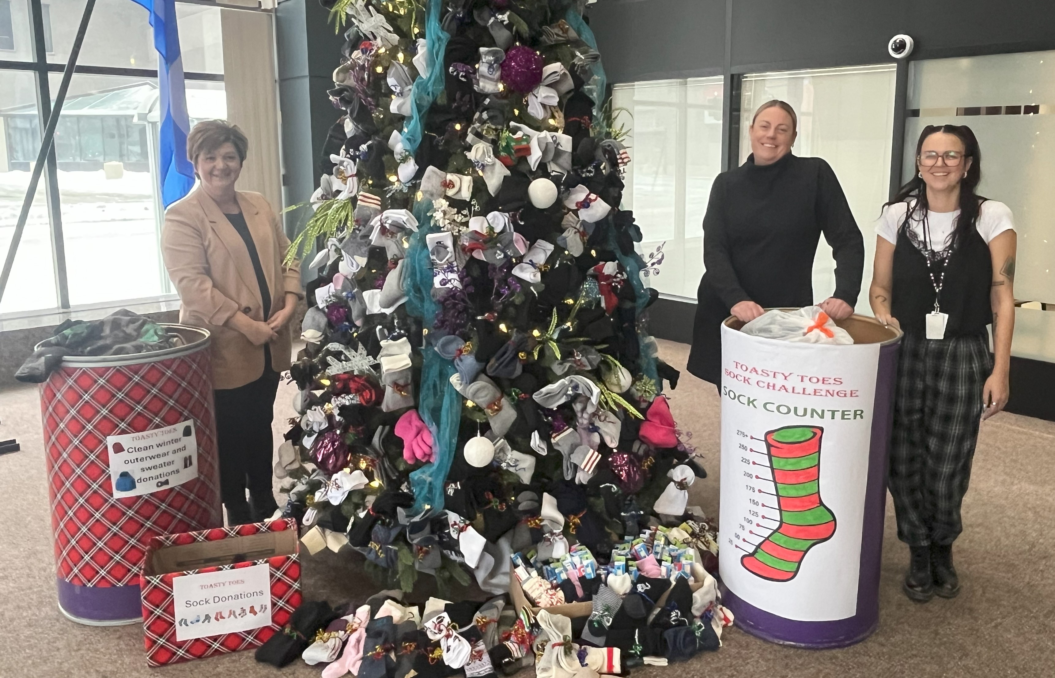 Three people stand by a Christmas tree