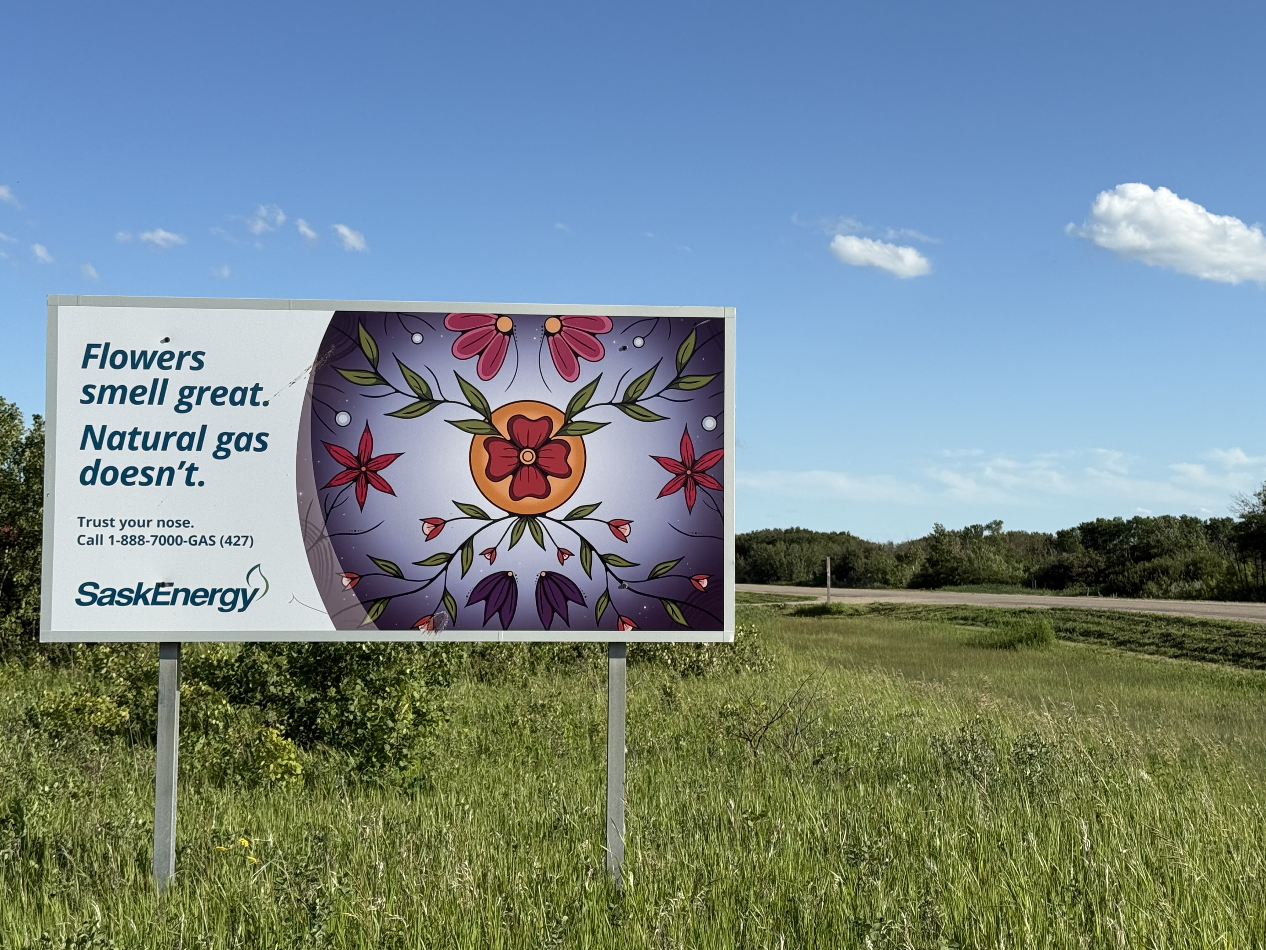 SaskEnergy safety sign with Indigenous art in field.
