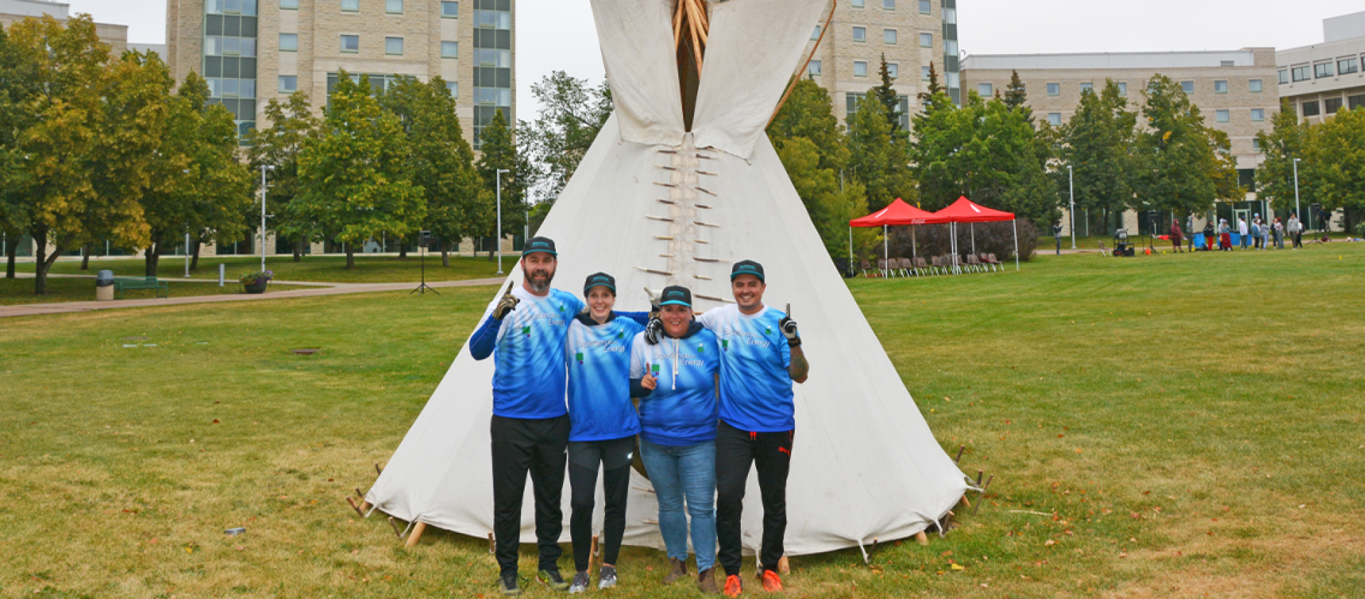 Four employees wearing matching blue shirts stand in front of the tipi they built. 
