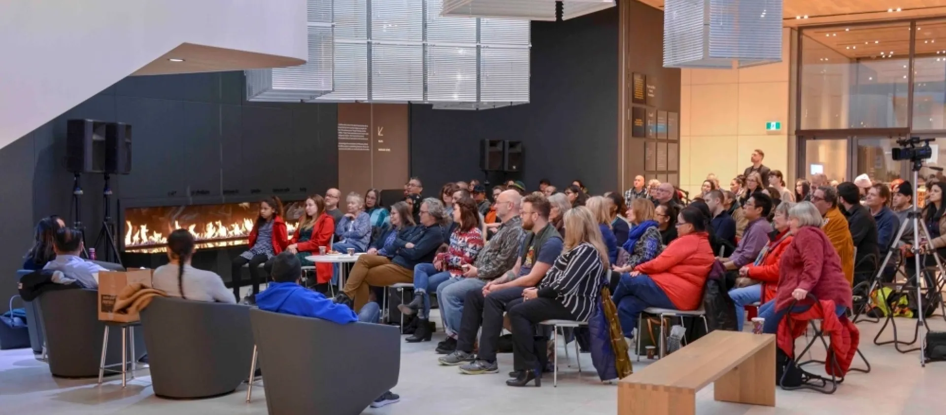 People sit in chairs, gathered around a fireplace at the Remai Modern gallery. 