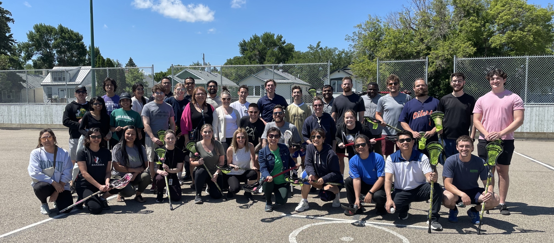 A group of people pose on a concrete surface, each holding lacrosse sticks.