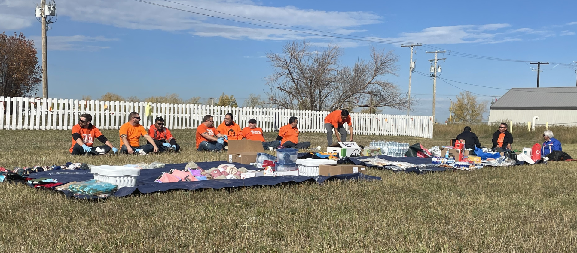 Two tarps containing food and household items are laid out in a field. 