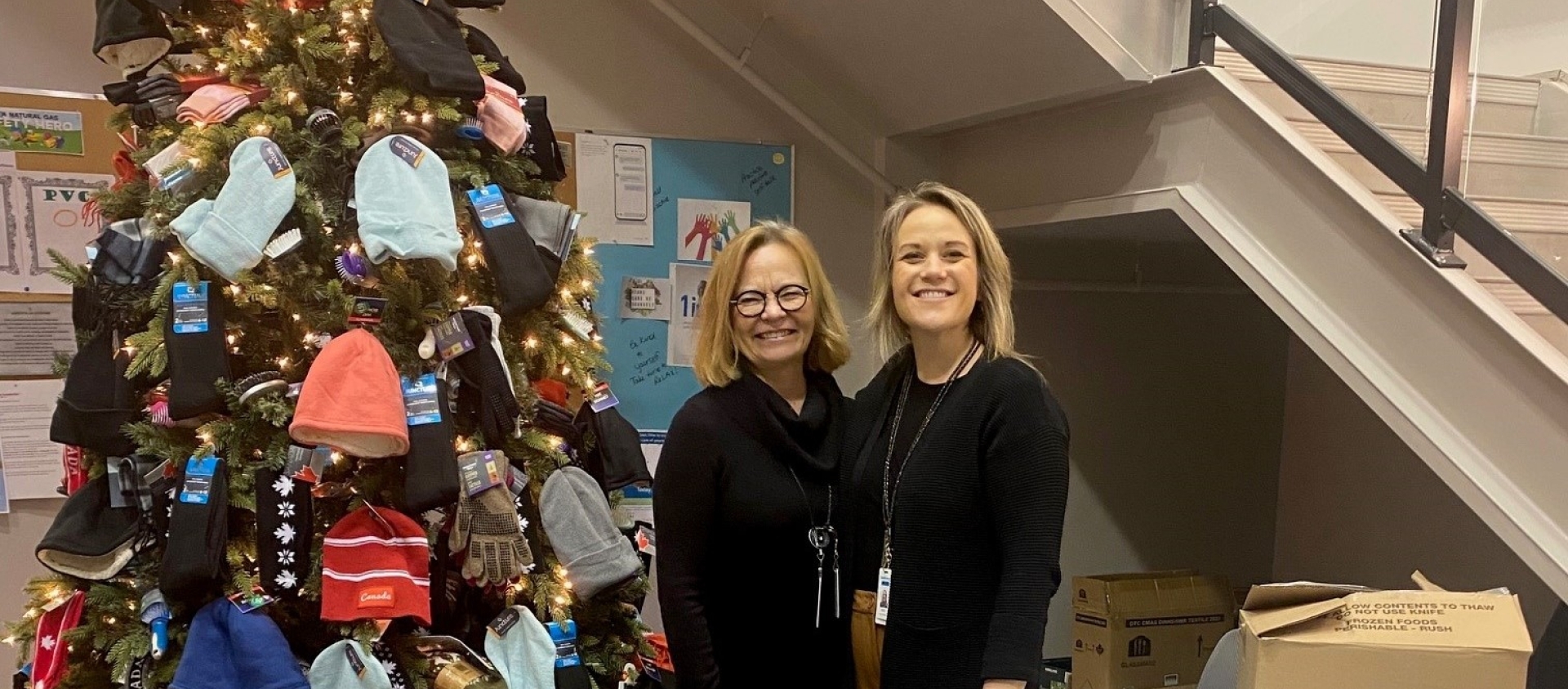 Two people stand next to a Christmas tree. 