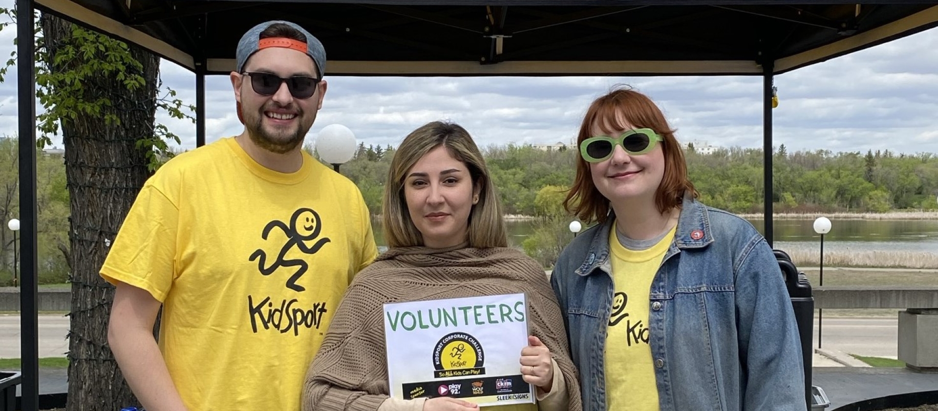 Three people stand in front of a KidSport tent