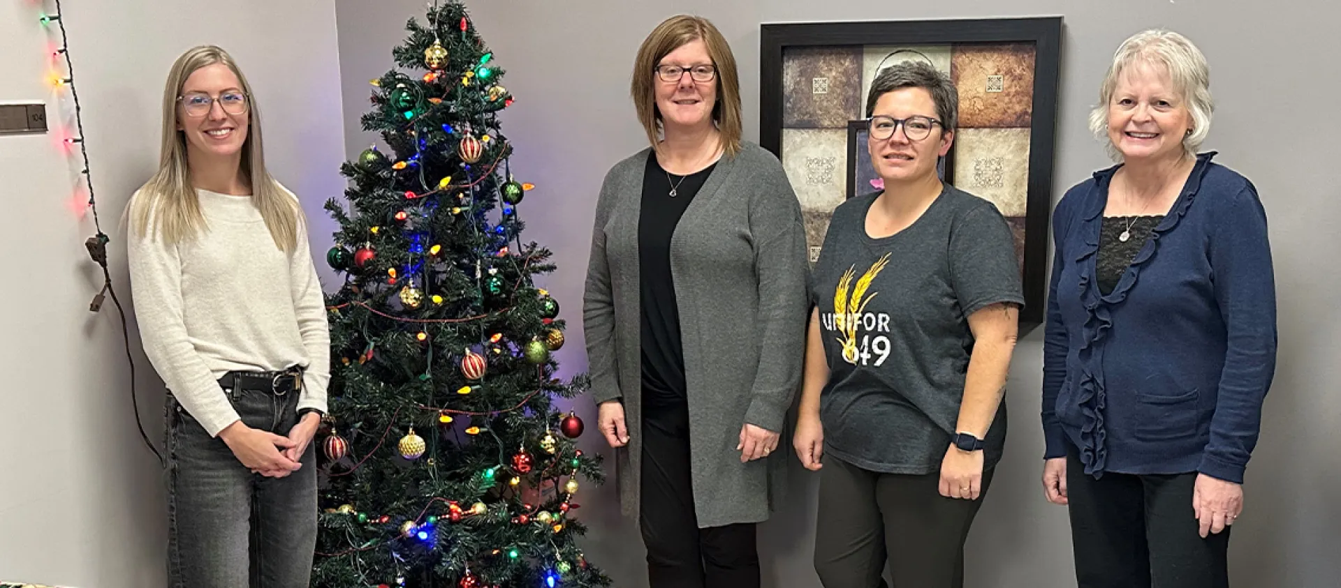 Four people stand near a Christmas tree