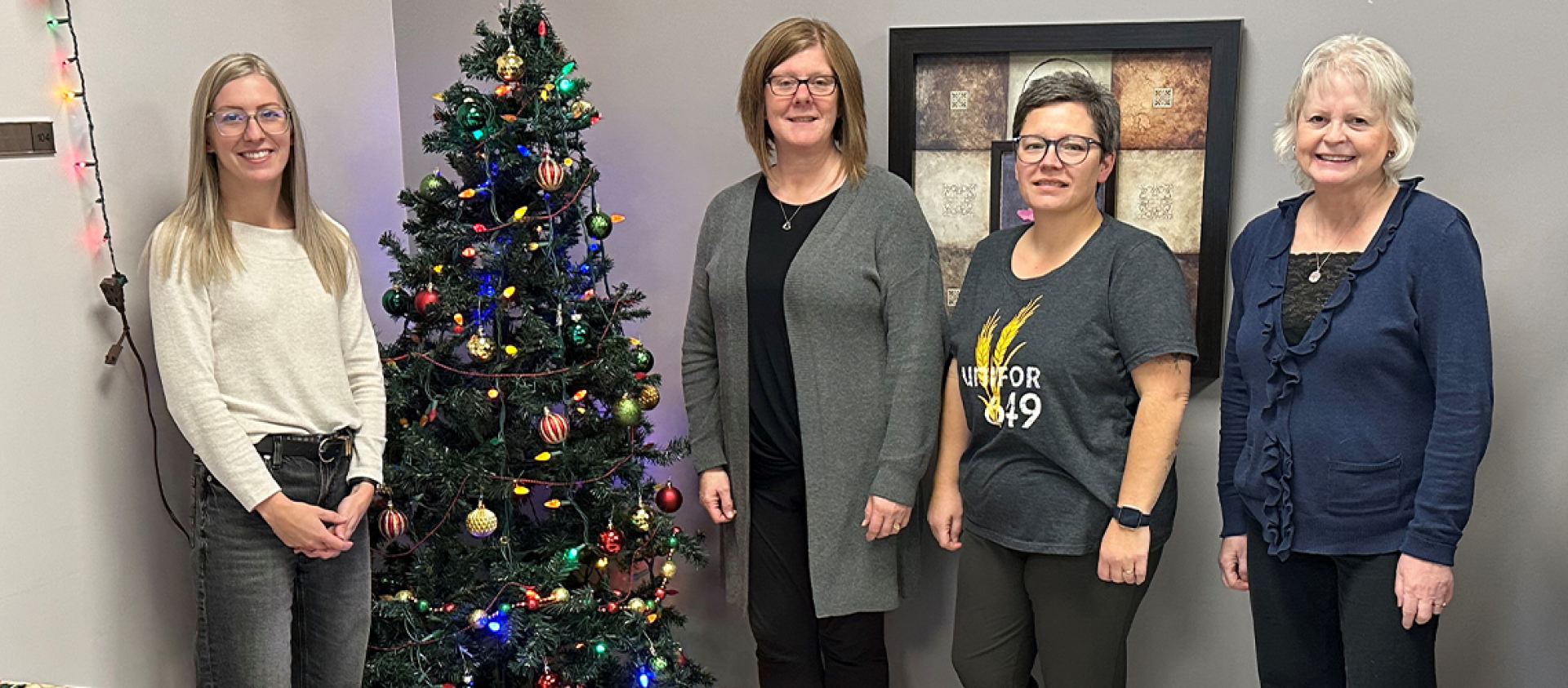 Four people stand near a Christmas tree