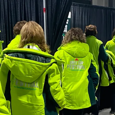 Ten volunteers all wearing matching bright green "Grey Cup Festival" jackets line up to register for their shift. 