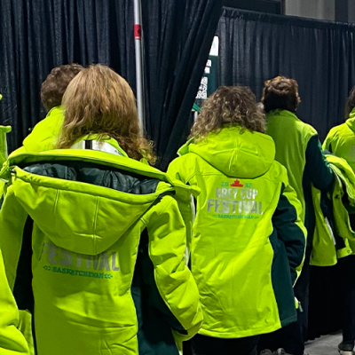 Ten volunteers all wearing matching bright green "Grey Cup Festival" jackets line up to register for their shift. 