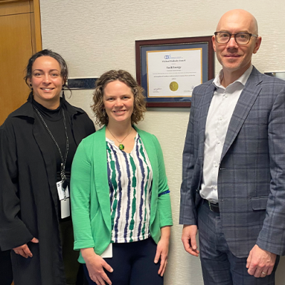 Three SaskEnergy employees smile, with the framed award certificate on the wall behind them. 