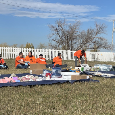 Two tarps containing food and household items are laid out in a field. 