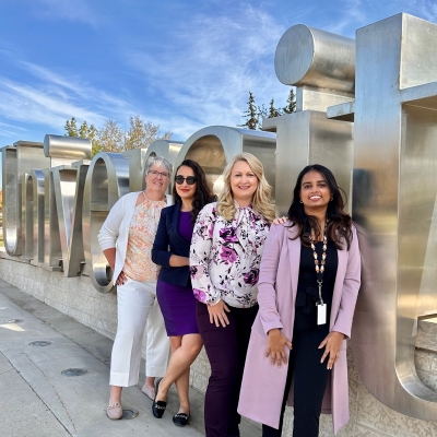 Four people stand in front of a University of Regina sign