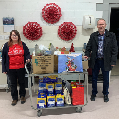 Two people stand on either side of a cart full of bags and boxes of food donations.