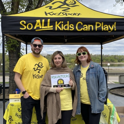 Three people stand in front of a KidSport tent