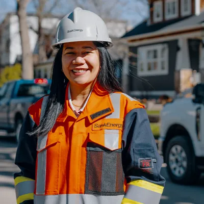 A woman with long dark hair in orange and blue safety gear and a grey hard hat stands in front of a SaskEnergy truck. A Canada's top 100 employers logo is on the left of the image. 
