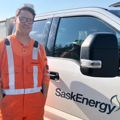 A SaskEnergy technician stands in front of a white truck.