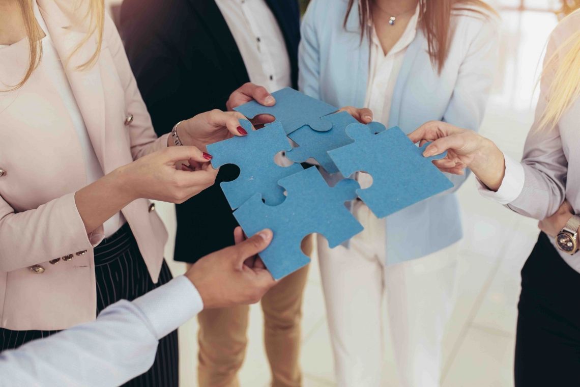 Businesspeople joining puzzle pieces in office Businesspeople joining puzzle pieces in office