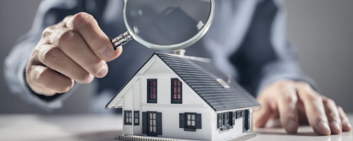 Hand with magnifying glass inspecting house