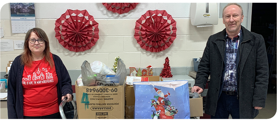 Two people stand on either side of a cart full of bags and boxes of donated food items. 