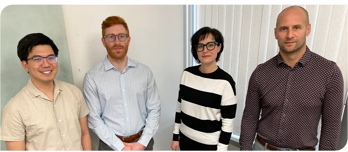 Four people in a row. The image is cut off to show just their upper bodies. 