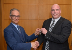 Two people shake hands while holding a medal.