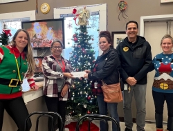 A person hands over a cheque to another person while three people stand beside them.