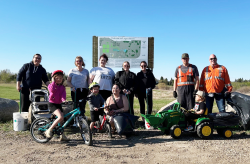 Eight adults stand in a row, with three children on bikes and riding toys in front of them.