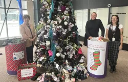 Three people stand by a Christmas tree