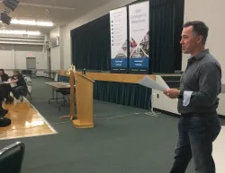A person standing at the front of the room speaking to a crowd
