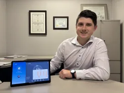 A man sits at a desk holding a digital tablet displaying the app for adjusting his smart thermostat.