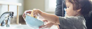 Child and parent washing dishes in sink