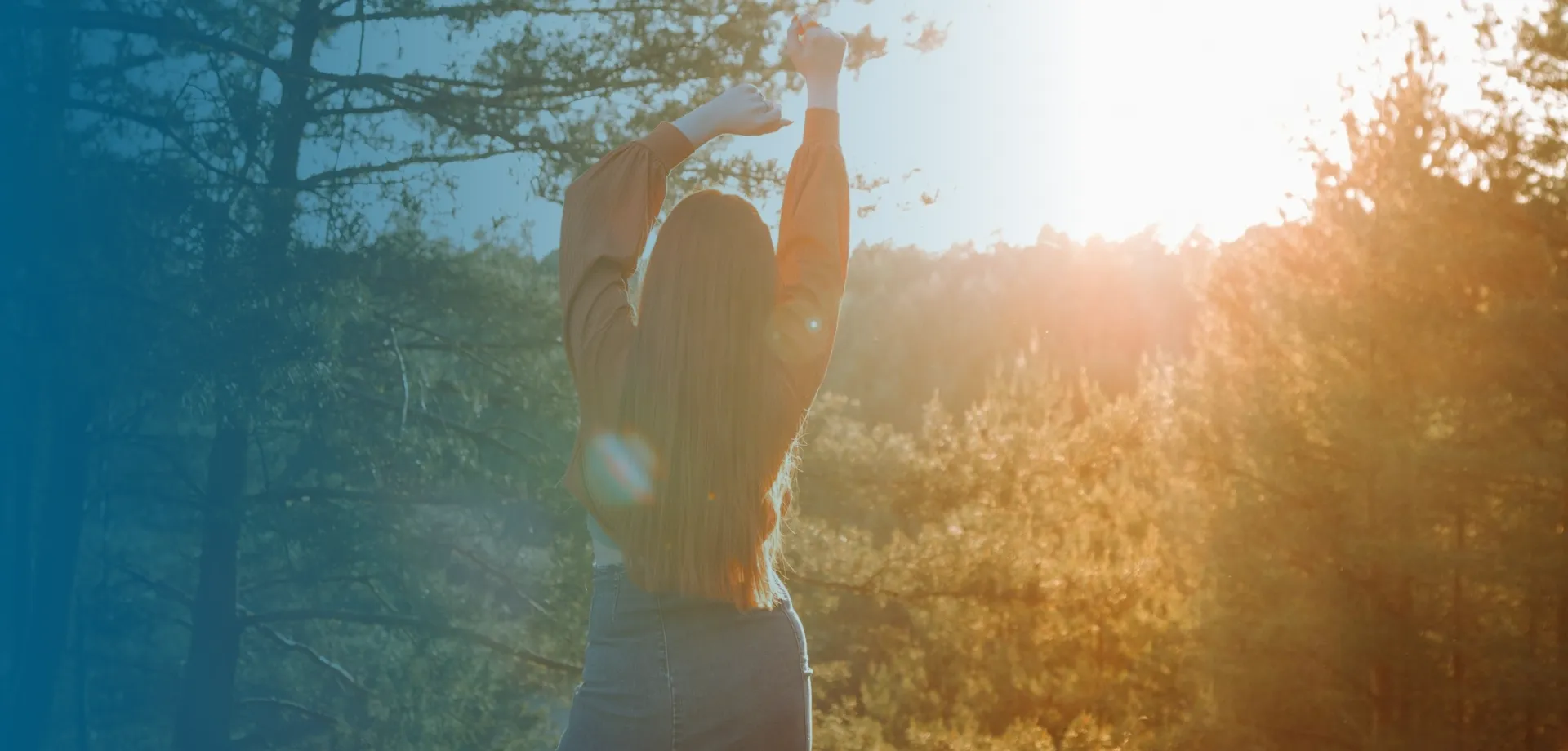 woman in orange shirt walking into the sunset with arms above head
