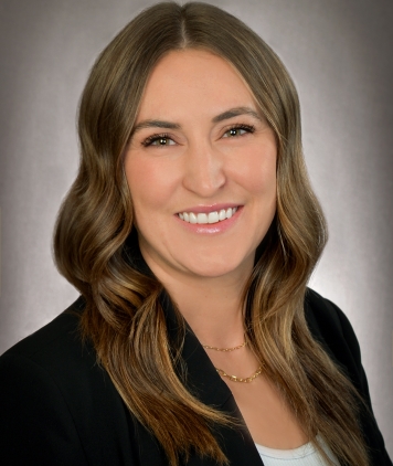 A woman with long light brown hair smiles, wearing a black jacket and white top. 